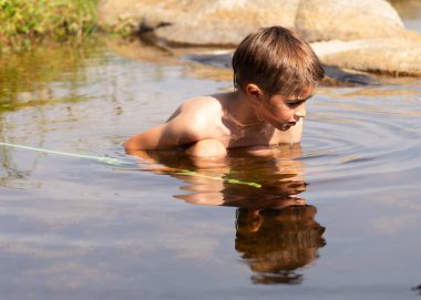 Doğal bir havuzda yıkanan çocuk bir şeye bakıyor.