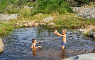 Yazın doğal havuzda su sıçratmaca oynayan iki çocuk.