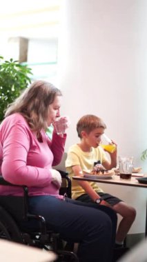 Tekerlekli sandalyede beyaz bir büyükanne ve bir restoranda birlikte yemek yiyen bir torun. Özürlü insanlar