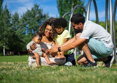 Çocuklu Latin bir aile ve bir bebek parkta birlikte oturuyorlar.