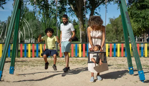 İki çocuklu bir aile, bir çocuk ve bir bebek çocuk parkında salıncakta sallanıyor.