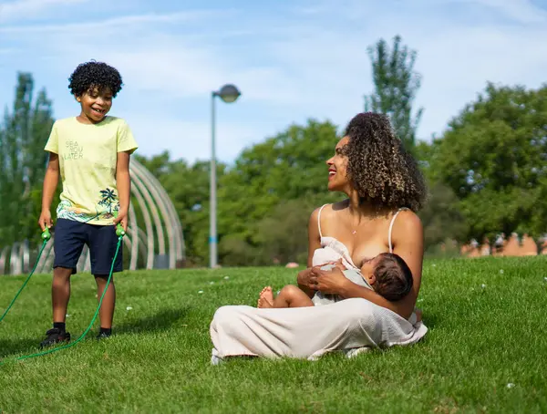 stock image Latin mother with her 7-year-old son and breastfeeding her 6-month-old baby in a park. Venezuelan family. Family with afro hair