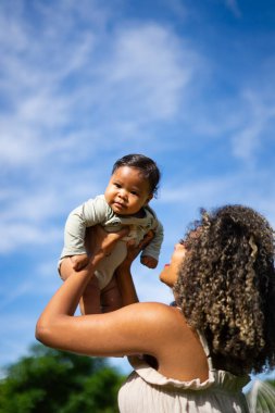 6 aylık Latin bebeğini kaldıran afro saçlı Latin bir anne.