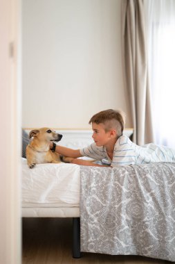 Çocuk yatak odasında köpeğini okşuyor.