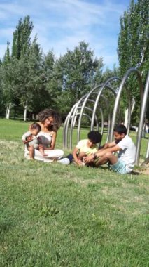 Çocuklu Latin bir aile ve bir bebek parkta birlikte oturuyorlar.