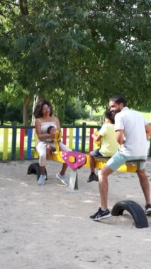 Latin ailesi ve 8 yaşındaki oğulları bir çocuk parkında salıncakta birlikte oynuyorlar.