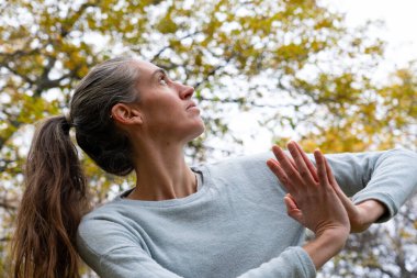 Orta yaşlı beyaz bir kadının portresi. Sonbaharda ormanda yoga ve meditasyon yapıyor.