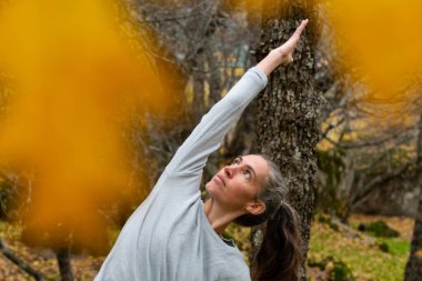 Sonbaharda huzurlu bir ormanda yoga yapan bir kadın.