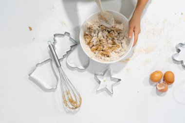 Yukardan görülebilen ev yapımı kurabiye hamuru kâsesi ve kopyalanmış Noel kurabiyeleri yapmak için Noel şekilli kalıplar. Çocuk Noel kurabiyesi pişiriyor.