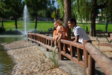Baba, anne ve 1 yaşındaki bebek parktaki ördekleri izliyorlar.