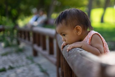 1 yaşında Latin bir bebek. Parkta çitten eğilmiş meraklı bakıyor.