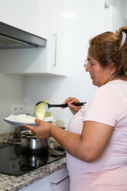 Orta yaşlı Latin bir kadın evdeki mutfakta patates püresi servis ediyor.