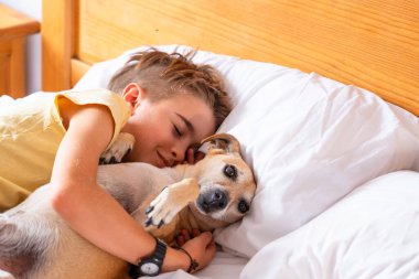 Çocuk odasında köpeğine sarılıyor.