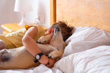Odasında köpeğiyle yatağında yatan bir çocuk.