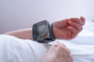 Yatakta yaşlı bir kadının tansiyonunu yüksek tansiyon monitörüyle ölçtüğü bebek.