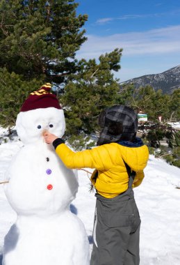 Tanınmayan bir çocuk dağda bir kardan adamın burnuna havuç sokuyor.