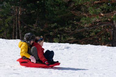 İki çocuk kızak sürerken eğleniyor. Bir fotokopi aletiyle yamaçtan kayıyor.