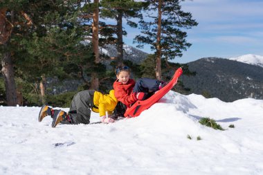Arka planda karlı dağlarla gülen kızakla oynayan iki çocuk.