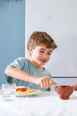 Happy Caucasian boy eating a plate of pasta with tomato at home with copy space clipart