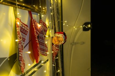 Noel kıyafeti giymiş çocuk, Noel ışıkları ve çoraplarıyla donatılmış olarak karavandan dışarı bakıyor.