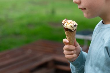 Güneşli bir yaz gününde lezzetli bir dondurma külahını tutan ve yiyen çocuk.