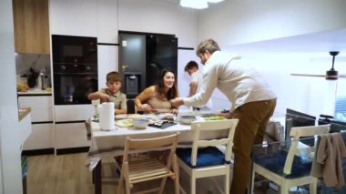 Aile, modern mutfakta birlikte akşam yemeği yiyor.