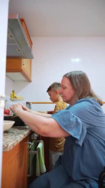 Tekerlekli sandalyedeki kadın mutfakta çocukla yemek hazırlıyor.