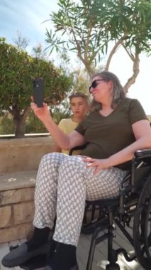 Tekerlekli sandalyedeki büyük anne torunuyla yavaş çekimde selfie çekiyor.
