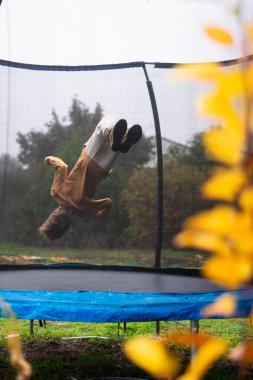 Çocuk bulutlu bir sonbahar gününde trambolinde ters takla pratiği yapıyor.