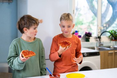 Işıl ışıl yanan bir mutfakta basit bir tost ve reçel kahvaltısının tadını çıkaran iki genç kardeş.