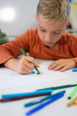 İlkokul öğrencisi renkli kalemlerle çizim yapmaya, sanat eğitiminde yaratıcılık ve iyi motor beceriler geliştirmeye odaklanmış.