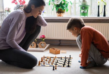 Anne oğluna satranç oynamayı öğretiyor, evdeki satranç tahtasına konsantre oluyor.