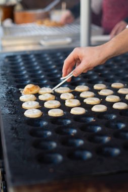 Şef, açık hava pazarında sıcak bir ızgarada yemek pişirmek için maşa kullanıyor.