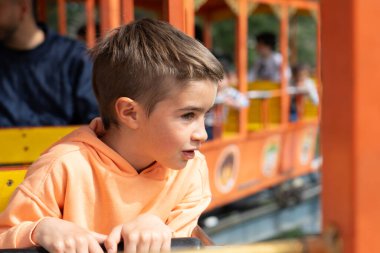 Genç bir çocuk lunaparkta tren yolculuğunun keyfini yaşıyor, manzara ve sesleri alıyor.