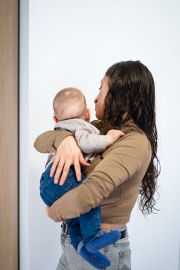 Anne, küçük oğlunu kucaklarken oturma odasında dikiliyor.