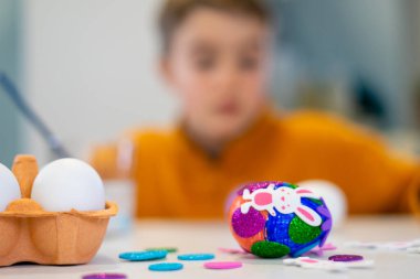 Renkli paskalya yumurtası. Arkaplanda bulanık çocukla birlikte masanın üzerinde sim ve tavşan etiketleriyle süslenmiş.