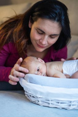 Sevgi dolu bir anne yeni doğmuş bebeğini okşuyor hasır bir sepetin içinde uzanıyor ve hassas bir annelik anının tadını çıkarıyor.