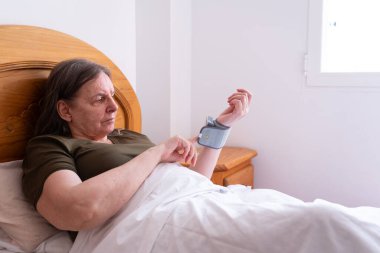 Senior woman checking blood pressure with an electronic device clipart