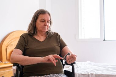 Senior woman in a wheelchair checking her smartphone indoors clipart