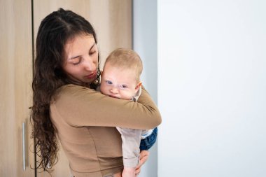 Sevgi dolu anne, sıcak bir odada neşeli bebeğini kucaklıyor.