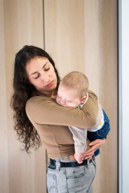 Genç Latin anne, rahat bir evde uyuyan bebeğini kucaklıyor.