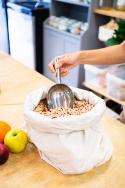 Dükkan sahibi, sıfır atık bakkalındaki çuval bezinden Borlotti fasulyesi toplamak için metal kepçe kullanıyor.