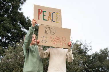 Barış ve savaşı protesto eden çocukların elinde mukavva tabelalar var.