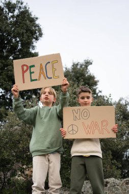 Barış ve savaşı protesto eden çocukların elinde mukavva tabelalar var.