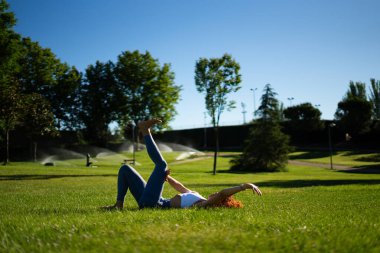 Güneşli bir günde yeşil parkta hipopresif pozlar veren bir kadın.