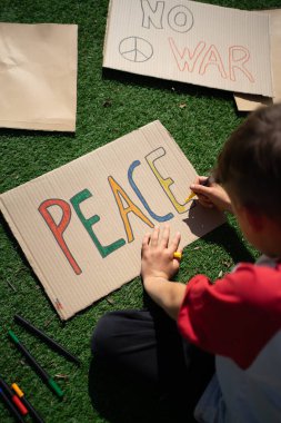 Kartona renkli barış sloganları çizen çocuk, barış gösterisine hazırlanıyor.