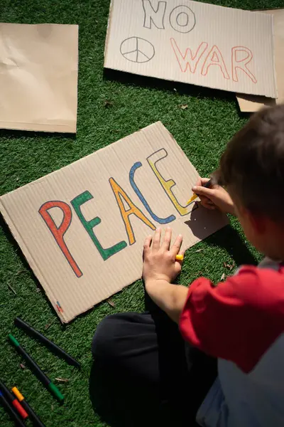 Kartona renkli barış sloganları çizen çocuk, barış gösterisine hazırlanıyor.