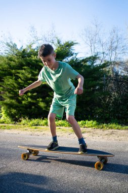 Güneşli bir günde, banliyö sokaklarında sörf yapan, açık hava aktivitelerini seven ve denge becerilerini geliştiren çocuk.
