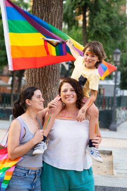 Mutlu lezbiyen anneler ve oğullarının gökkuşağı bayrağı ve tabloları gay gururunu kutluyor.