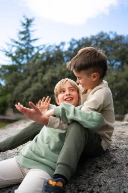 İki kardeş bir kayanın üzerinde oturuyor, birlikte oynuyor ve dışarıda vakit geçiriyorlar.